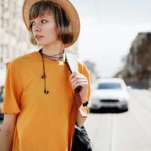 Young girl with headphones in a yellow T-shirt and a straw hat walks with a backpack along a city